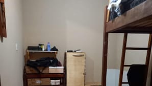 Una habitación pequeña y poco amueblada con una cama individual superpuesta, un escritorio de madera con silla y un mueble bajo.
