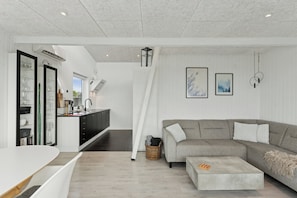 A modern living room with a grey sectional sofa, a white coffee table, and a kitchen area with a black countertop and white cabinets.