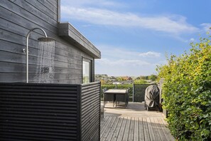 Een houten terras met een inbouwdouche, zitplaatsen buiten en uitzicht op de omgeving.
