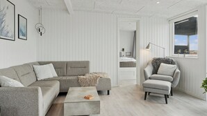 Ein modernes Wohnzimmer mit einem grauen Sofa, einem kleinen Hocker, einem Couchtisch, einem Sessel und einem Fenster mit Blick.