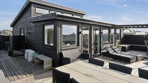 Eine Dachterrasse mit Glasumrandung, Sitzgelegenheiten im Freien und Blick auf die Stadtlandschaft.
