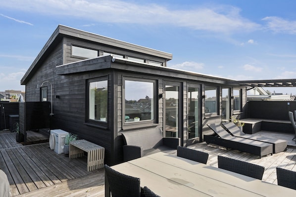 A rooftop deck with a glass enclosure, outdoor seating, and a view of the cityscape.