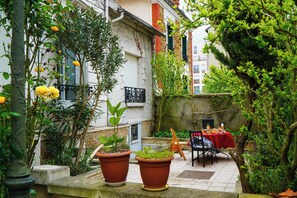 A courtyard with potted plants, a table with a red tablecloth, and a chair. - Cosy new studio 2 min RERB (Aulnay-sous-Bois)