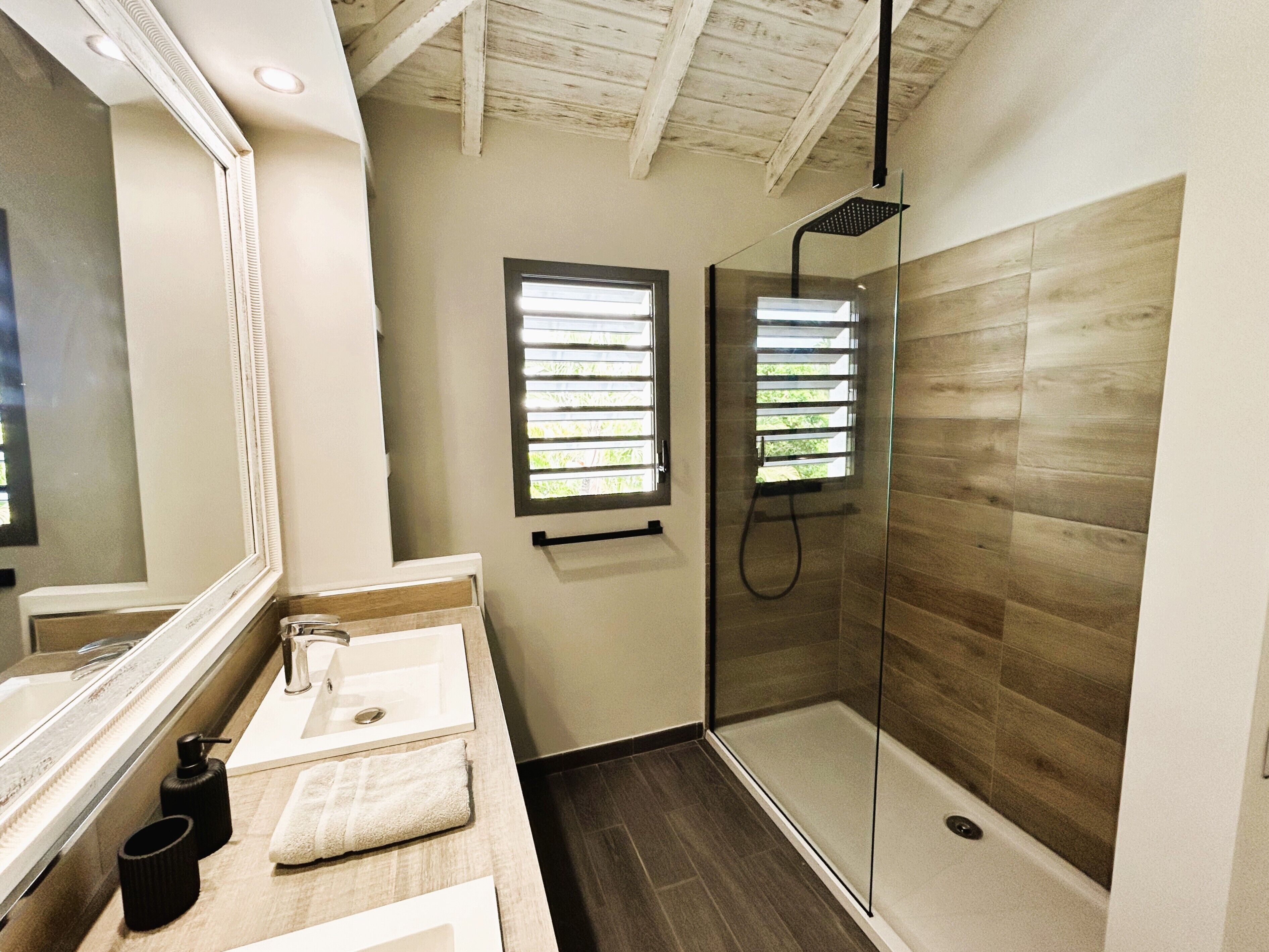 A modern bathroom with a glass-enclosed shower, a large mirror, and a wooden vanity.