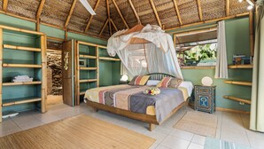 Een kamer met een bed, een plafondventilator, een nachtkastje en een raam met uitzicht op groen.