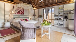 Een slaapkamer met een bed, een rieten stoel, een nachtkastje met een bloevas en een plafondventilator.