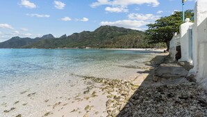 Een kuststrand met helder water, een rotsachtige kustlijn en een berg op de achtergrond.