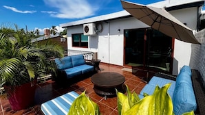 A patio with a blue sofa, a round table, and large green plants.