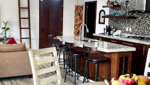 A modern kitchen with a central island, bar stools, and a dining table.