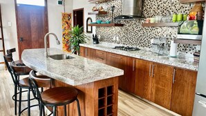 A modern kitchen with a central island, bar stools, wooden cabinets, and a tiled backsplash.