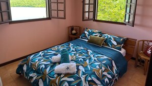 Ein Schlafzimmer mit einem Bett, zwei Nachttischen, einem Fenster mit Rollläden und einer Klimaanlage.