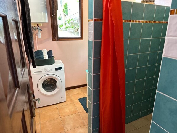 Ein kleines Badezimmer mit Waschmaschine, Duschvorhang und Fliesenwänden.