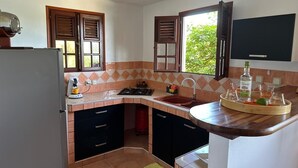 Een kleine keuken met een koelkast, fornuis, spoelbak en een raam met luiken.