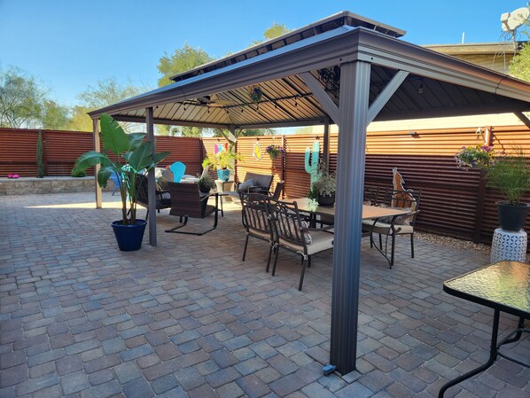An outdoor patio with brick flooring, metal furniture, and potted plants.