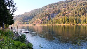 A serene lake with a dock, surrounded by lush greenery and forested hills. - Beautiful Clark Fork Riverside RV site (Clark Fork)