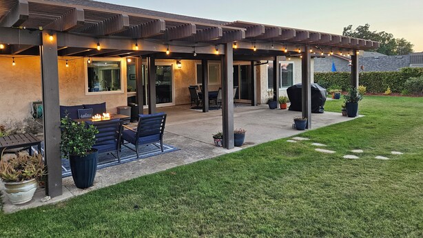 Una veranda riparata con posti a sedere all'aperto, un barbecue e luci decorative appese.