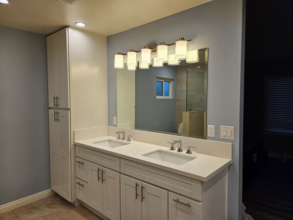 Une salle de bain avec un meuble-lavabo à deux vasques, un grand miroir et une fenêtre située au-dessus du miroir.