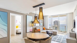 A modern hotel room with a dining area, a sofa, and a balcony with a city view.