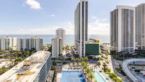 A high-rise hotel with a rooftop pool, surrounded by palm trees and a view of the ocean.