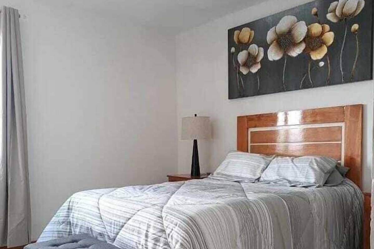 Un dormitorio con una cama grande, un cabecero de madera, un banco gris y un cuadro de flores en la pared.