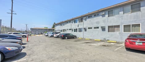 A parking lot with several cars, a building with multiple windows and air conditioning units, and a clear sky.