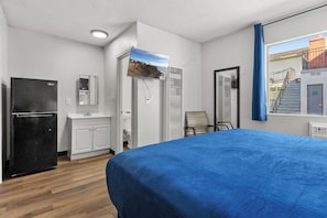 A hotel room with a bed, a refrigerator, a sink, a mirror, and a window with a view of a building. - Studio Lodge Hotel (North Hollywood)