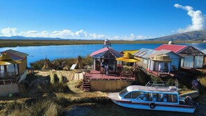 A lakeside settlement with multiple small buildings, a docked boat, and a clear view of the lake and distant mountains. - Little house on the floating islands of the Uros, Lake Titicaca, Puno-Peru (Puno)