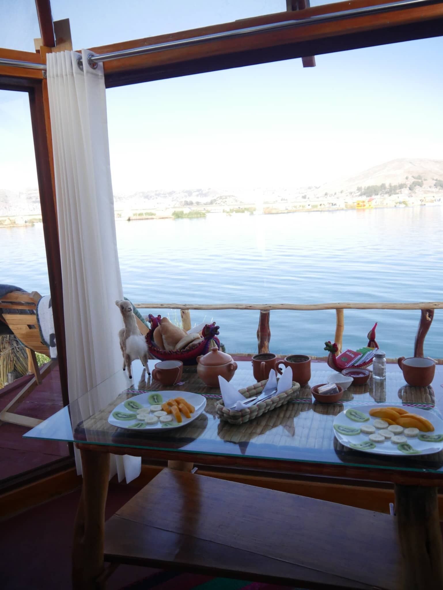 A table with a view of a calm lake, a wooden railing, and a table setting with plates of food and cups.