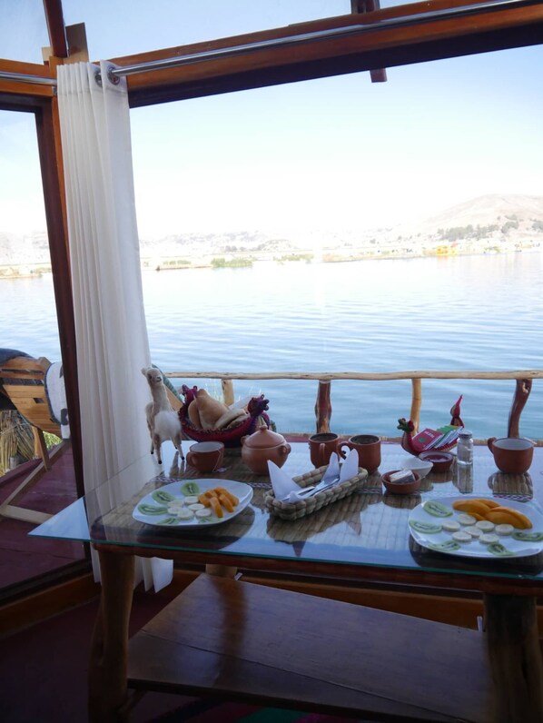 A table with a view of a calm lake, a wooden railing, and a table setting with plates of food and cups.