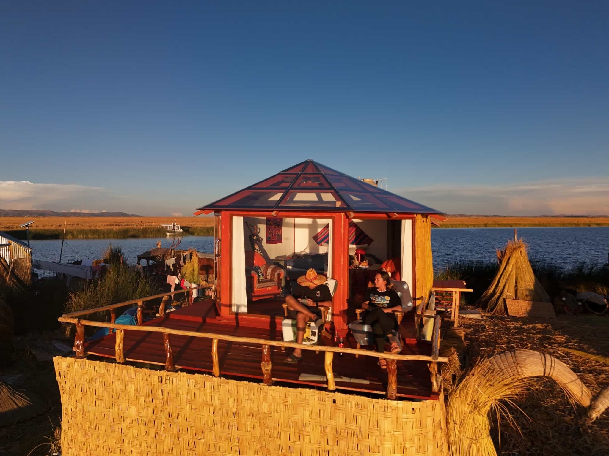 Una estructura pequeña, abierta, con techo rojo y una terraza de madera, con vista a un cuerpo de agua.
