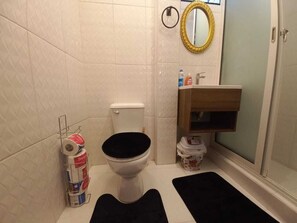 Ein Badezimmer mit Toilette, Waschbecken, Spiegel und Duschbereich.