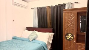 A bedroom with a bed, a wooden wardrobe, and a window with curtains. - Soothing 2-bedroom apartment with AC (GEORGETOWN)