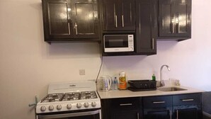 A compact kitchen with a stove, microwave, and dark cabinets. - Soothing 2-bedroom apartment with AC (GEORGETOWN)
