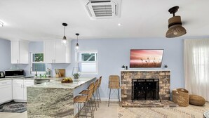 A modern kitchen with white cabinets, a marble island, and a stone fireplace.