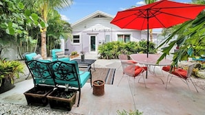 A patio with outdoor furniture, a red umbrella, and a house in the background.
