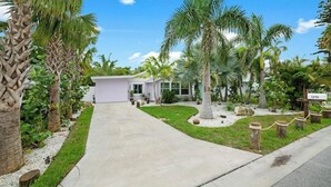 A residential property with a well-maintained lawn, palm trees, and a driveway leading to a house with a garage.