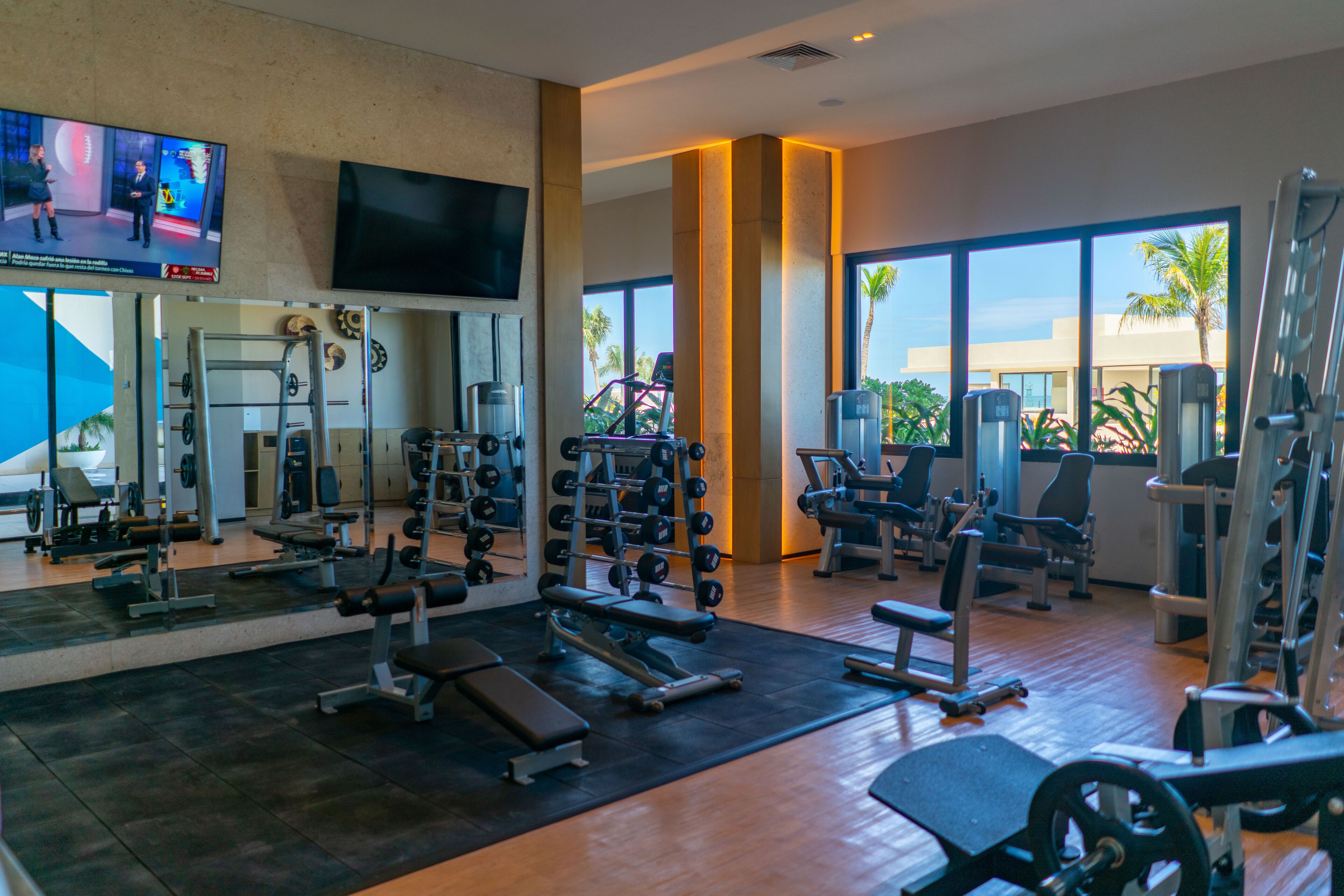 A gym with various exercise equipment, large windows, and a TV on the wall.