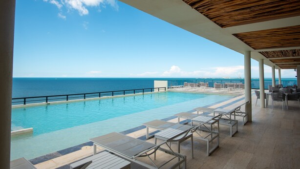 An infinity pool with a view of the ocean, lounge chairs, and a wooden ceiling. - Breathtaking 2BR deluxe condo with stunning views (Progreso)