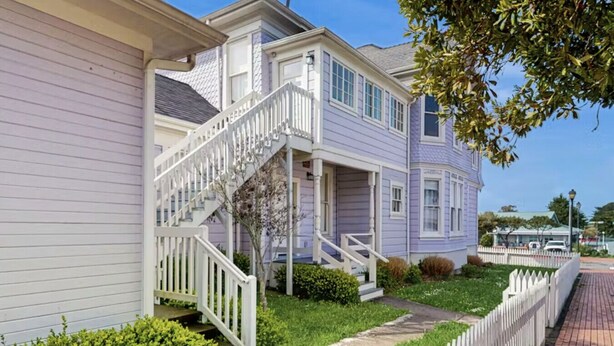 A two-story house with a white staircase leading to the front porch, surrounded by a white picket fence and green landscaping.