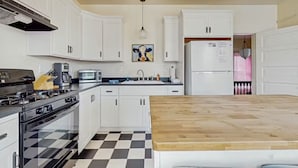 A kitchen with white cabinets, a wooden countertop, a stove, a microwave, and a refrigerator.