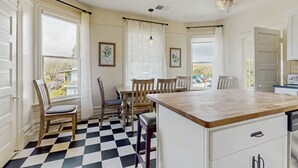 A kitchen with a checkered floor, wooden chairs, a central island, and white cabinetry.
