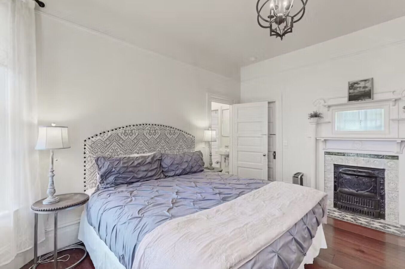 Une chambre à coucher avec un grand lit, une table de chevet avec une lampe, une cheminée et un miroir.