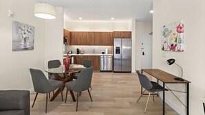 A modern kitchen with wooden cabinets, a stainless steel refrigerator, and a dining area with a glass table and grey chairs.