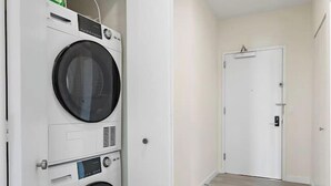 A laundry room with two front-loading washing machines and a dryer, a white door, and a hallway with a light-colored floor.