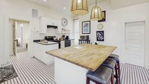Une cuisine moderne avec des meubles blancs, un îlot central en bois et des luminaires suspendus.