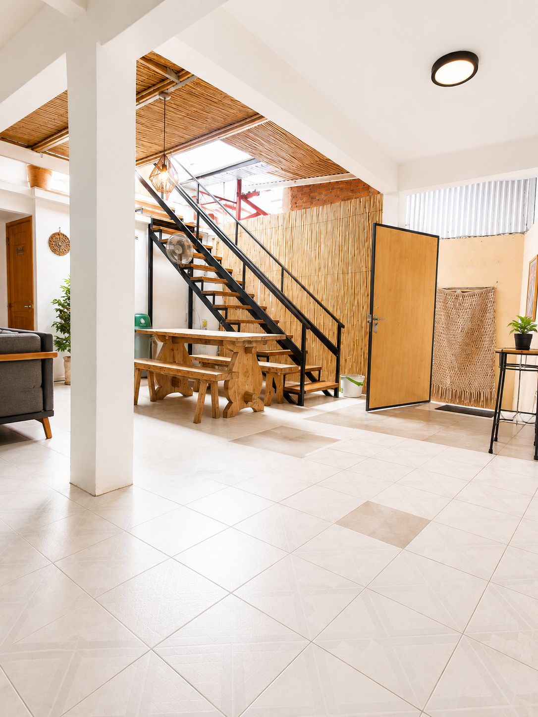 Une pièce spacieuse avec un escalier en bois, un coin repas avec des bancs et une grande fenêtre laissant entrer la lumière naturelle.