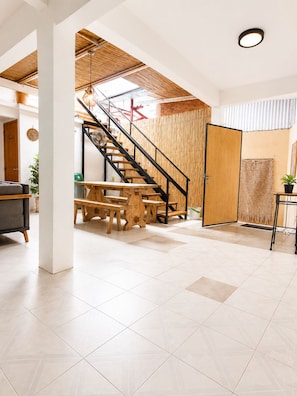 A spacious room with a wooden staircase, a dining area with benches, and a large window allowing natural light.