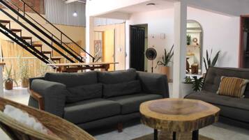 A spacious living room with a grey sofa, a round wooden coffee table, and a staircase leading to an upper level.