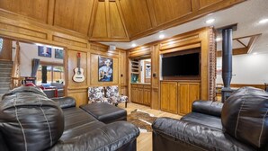 Un amplio salón con sofás de cuero, un televisor grande, paneles de madera y una chimenea.