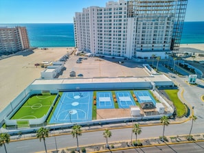 Um hotel à beira-mar com vários edifícios altos, um estacionamento e uma área de quadra esportiva.